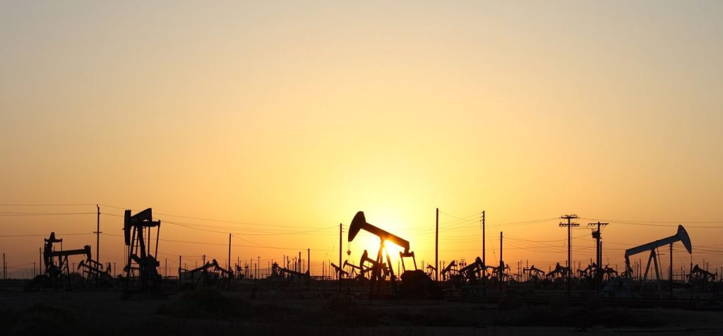 Oil Markets Balance Demand and Transition Photograph of oil pumpjacks silhouetted against a sunset sky.